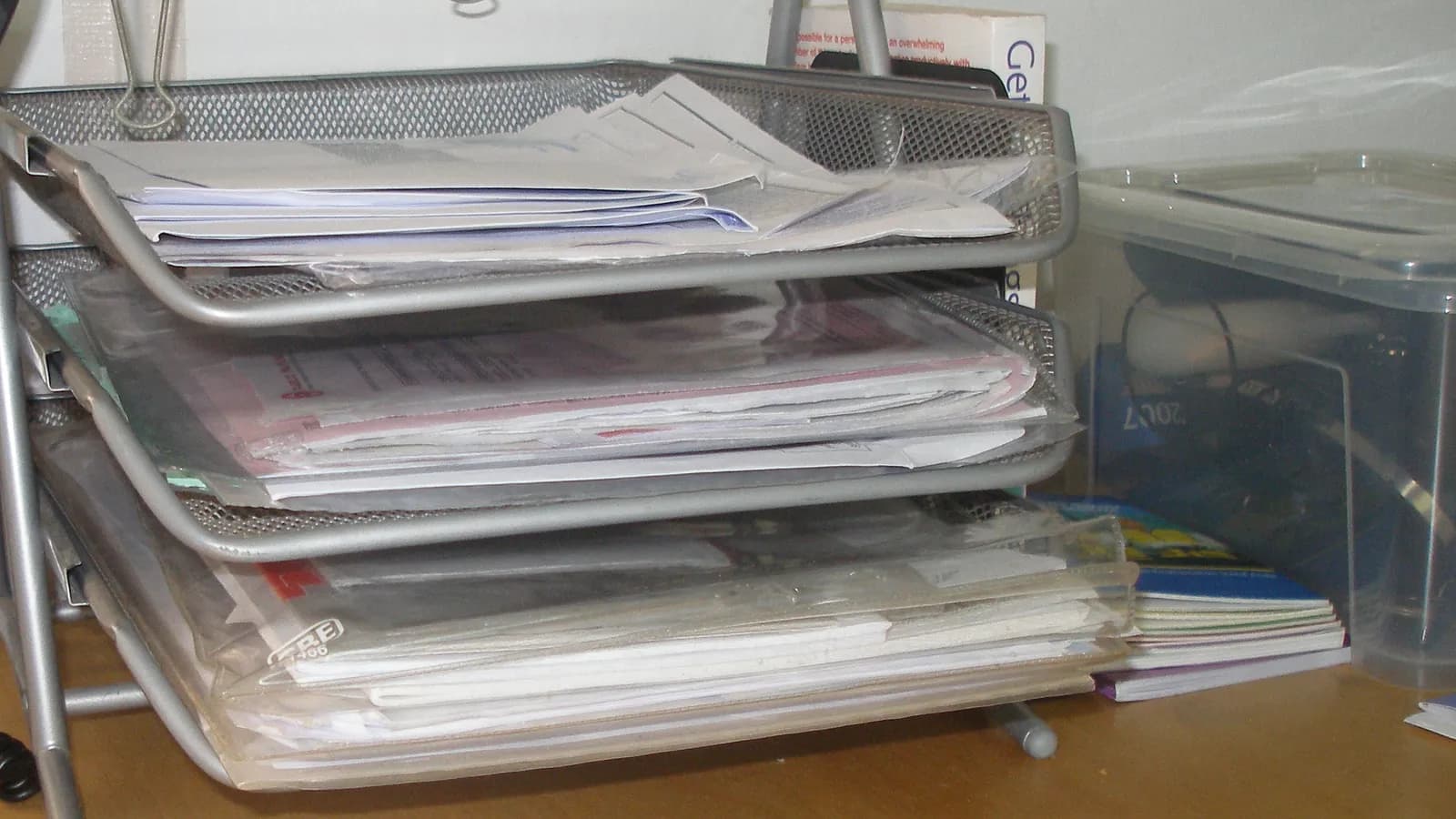 Bandejas de oficina metálicas llenas de papeles y documentos sin archivar sobre una mesa de madera