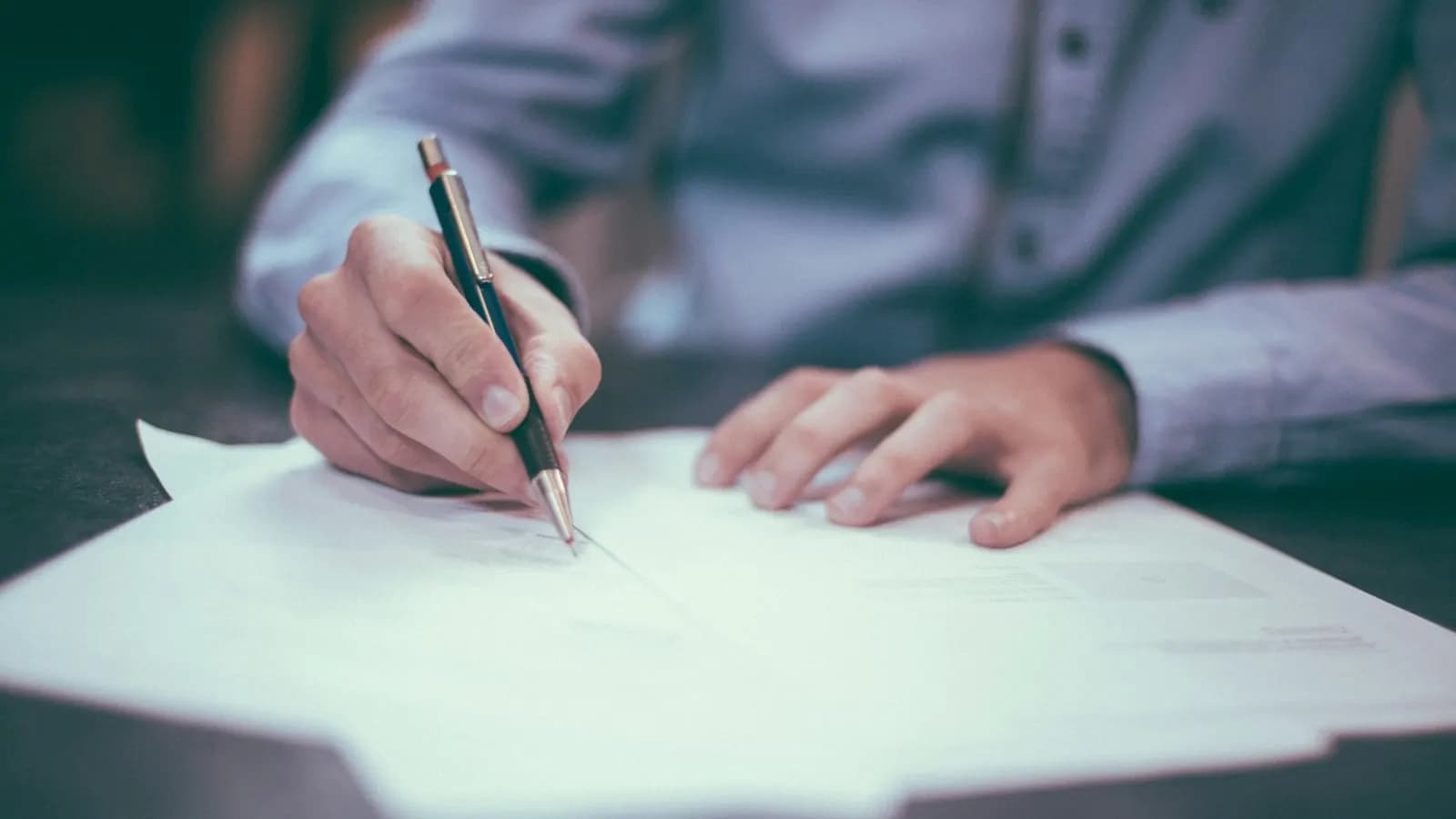 Persona escribiendo en un cuaderno junto a un portátil con datos financieros