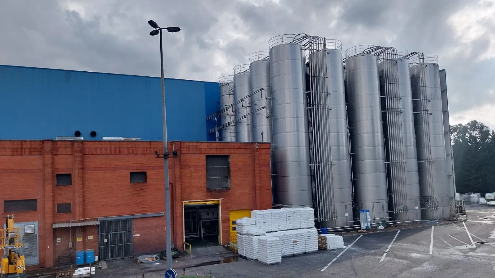 Patio de una fábrica de plásticos en Torrelavega, con silos metálicos, una nave azul y palés de sacos apilados