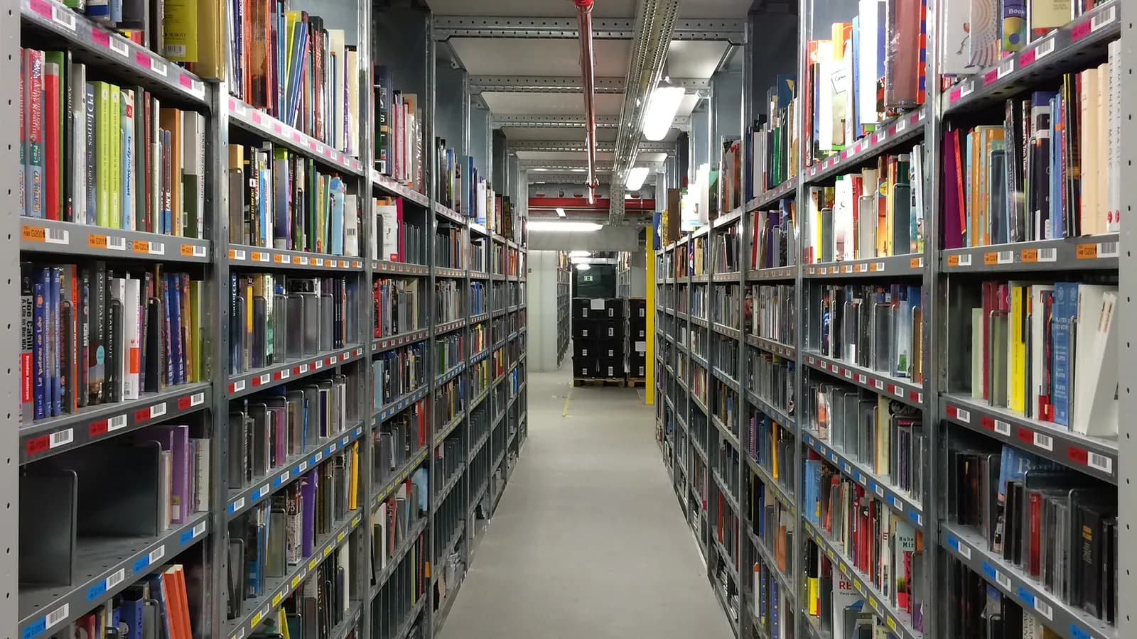Pasillo de un centro logístico entre estanterías metálicas llenas de libros y etiquetadas con códigos de barras, en San Fernando de Henares (Madrid)
